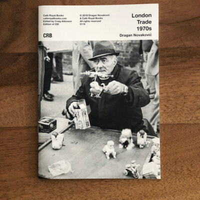 black and white cover man selling items out doors in hat and coat