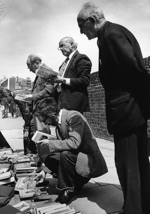 men looking at books from a second hand selection laid out in the street Club Row